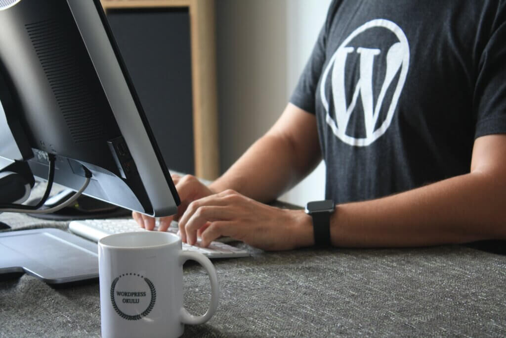 Person in black and white t-shirt with WordPress logo using laptop on table